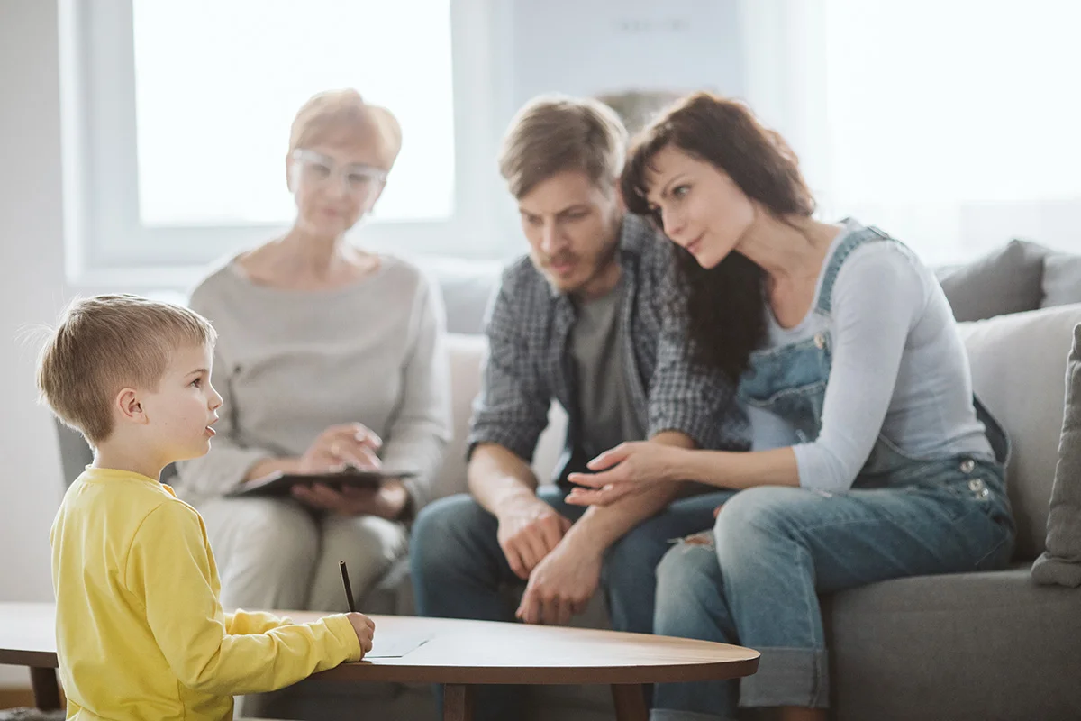 a child drawing on a table with a group of people sitting on the couch
