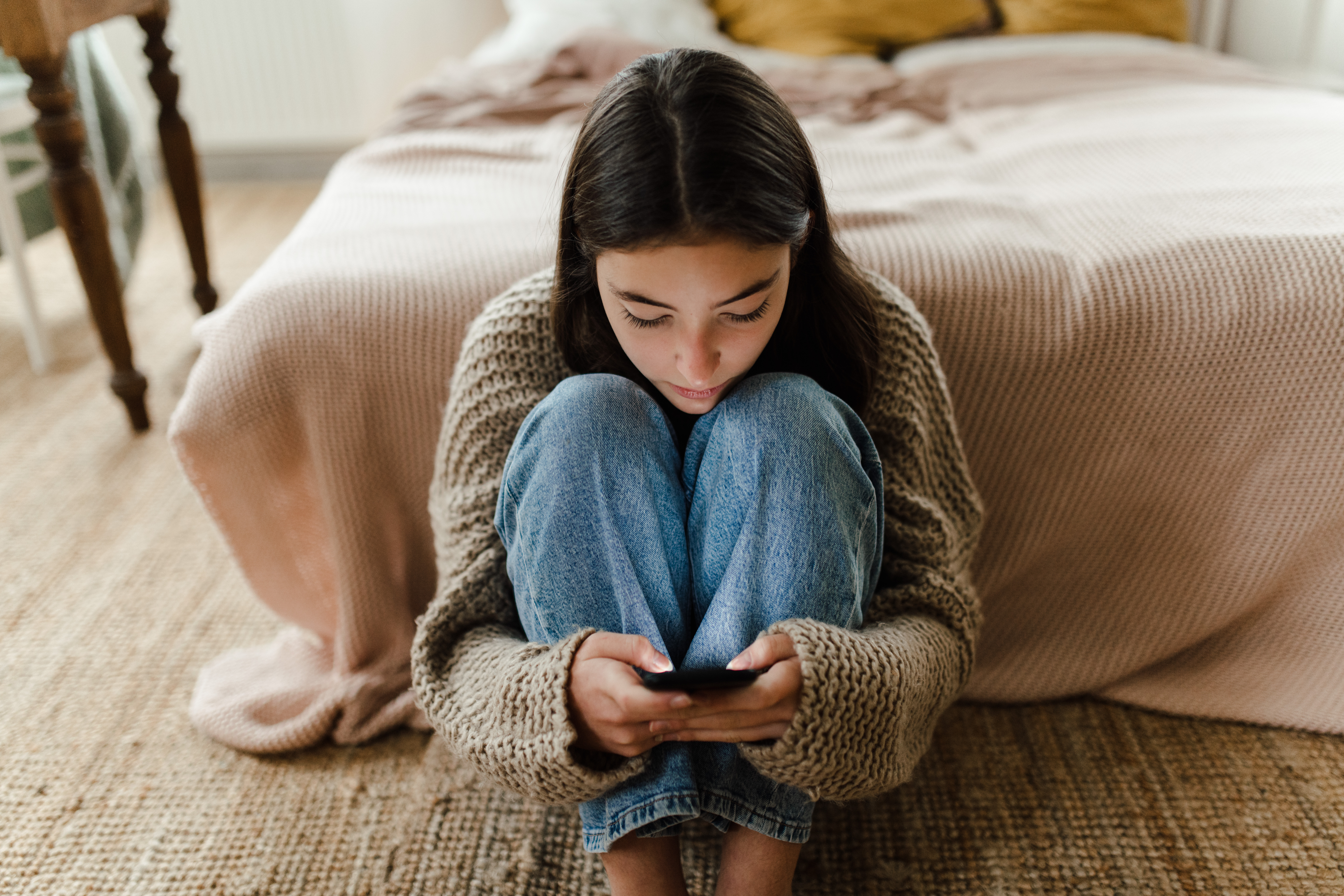 teen girl sits on the floor of her room on her phone