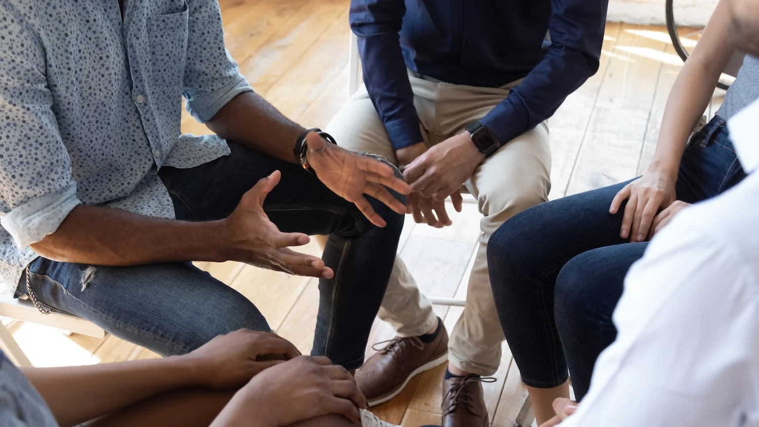 Close-up of people sitting in a support group circle, focusing on their hands and body language as one person gestures while speaking.